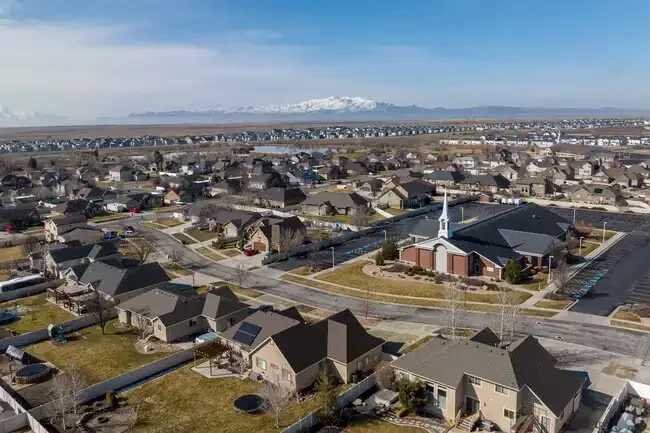 Aerial view of homes and a church in a Syracuse, Utah neighborhood with snow-capped mountains in the distance