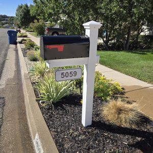 Professionally installed white vinyl mailbox post with a black mailbox and address plaque in a suburban landscaping bed