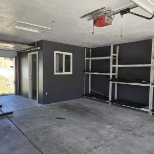 garage-finishing-and-restoration-salt-lake-city Newly finished and painted garage interior in Salt Lake City featuring charcoal gray walls, a white textured ceiling, and heavy-duty storage shelving.